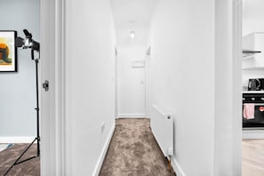 A narrow hallway with a radiator, a light fixture, and a kitchen area visible to the right. - Stylish Apartment - Netflix - On Street Parking (Birmingham)