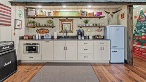 A kitchen with white cabinets, a refrigerator, a coffee maker, and various decorations including a sign that reads "Remington". - "The Florida Cracker "THE GREEN ROOM" READ our five stars review.. (Brooksville)