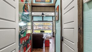 A hallway with a wooden floor, a ceiling fan, and a view of an outdoor area with a green lawn and a building in the background. - "The Florida Cracker "THE GREEN ROOM" READ our five stars review.. (Brooksville)