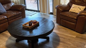 A living room with a round coffee table, leather sofas, and a wooden floor. - 4-Story Lake View Cabin with Boat Slip & Private Marina with Launch Ramp (Bass Lake)