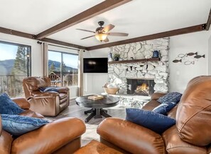 A spacious living room with leather sofas, a fireplace, a stone accent wall, and a television mounted above it. - 4-Story Lake View Cabin with Boat Slip & Private Marina with Launch Ramp (Bass Lake)