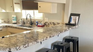 A kitchen with a marble countertop, a sink, and three black stools. - 4-Story Lake View Cabin with Boat Slip & Private Marina with Launch Ramp (Bass Lake)