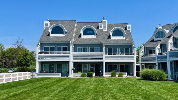 A large, two-story house with a symmetrical design, featuring a central entrance with a covered porch, large windows, and a well-maintained lawn. - Wonderful 3 Bedroom Condo in Beautiful Spring Lake, On the River (Spring Lake)