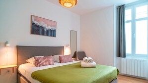 Una cama bien tendida con una manta verde, un cuadro en la pared y una ventana con cortinas.