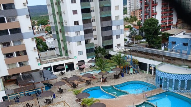 A rooftop pool area with multiple swimming pools, lounge chairs, and umbrellas. - Myapêcaldasnovas. (Centro Caldas Novas)