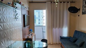 A compact living space with a dining area, a sofa, a TV, and a window with curtains. - Myapêcaldasnovas. (Centro Caldas Novas)