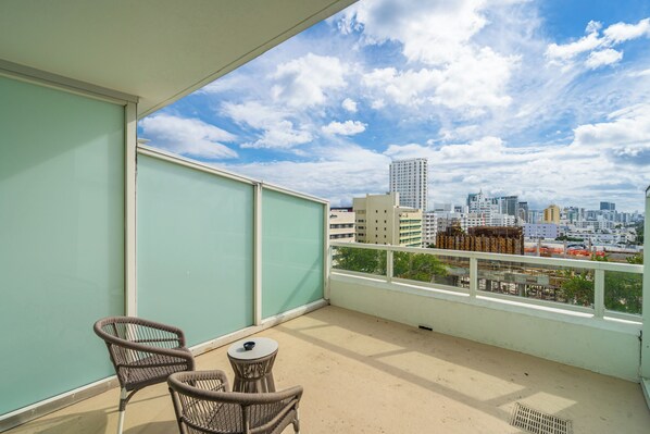Un balcone con due sedie in vimini e un tavolino, con vista su un panorama urbano e diversi edifici.