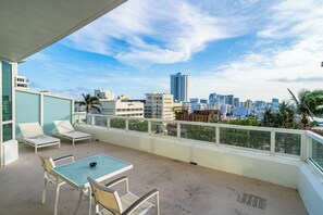 Un balcone con tavolo e sedie, che si affaccia su un panorama urbano con edifici e palme.