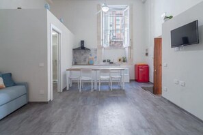 Un espace de vie compact comprenant un coin cuisine, un coin repas et un téléviseur fixé au mur.