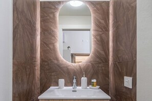 Une salle de bain dotée d’un meuble-lavabo en marbre, d’un évier et d’un miroir encadré par un arc architectural original.