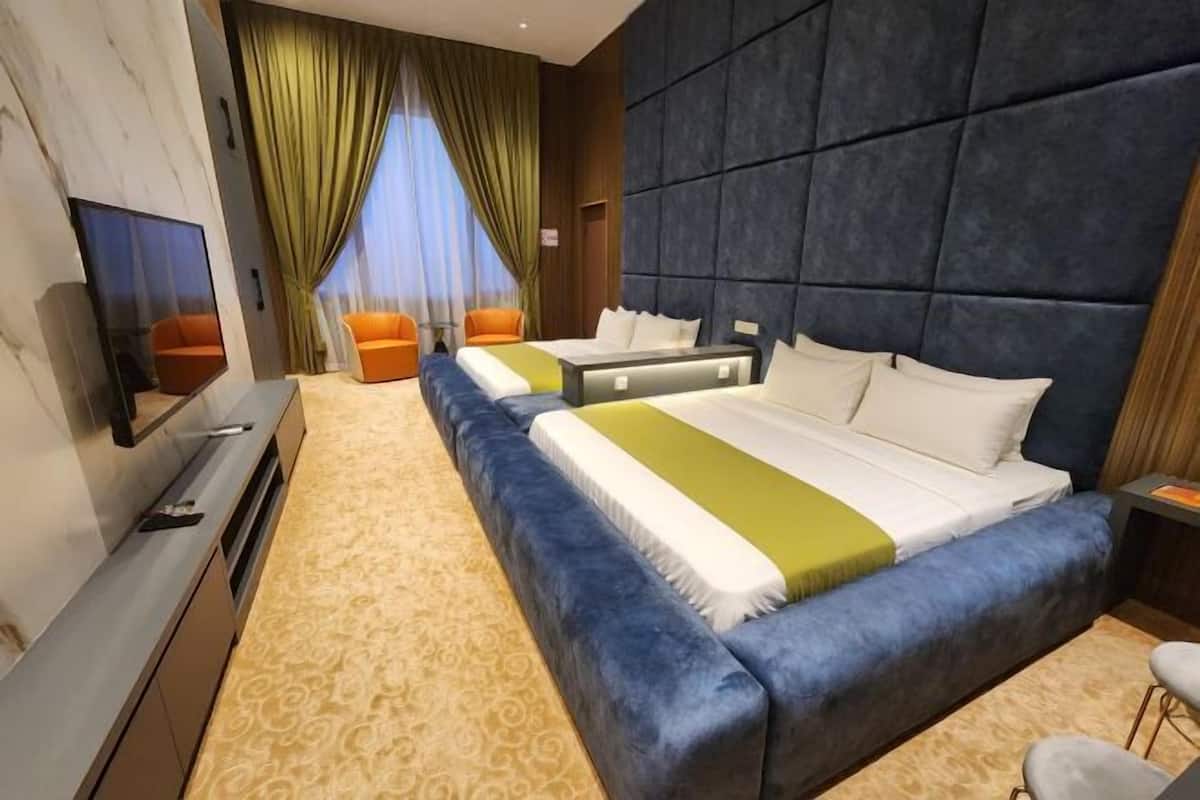 A hotel room with a large bed, two smaller beds, a TV, a desk, and a window with curtains.
