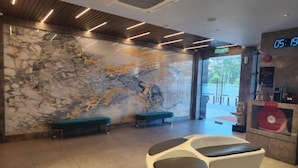 A lobby with a marble wall, a reception desk, and a digital clock displaying 05:19. - Hotel Marudu Inn (Kota Marudu)