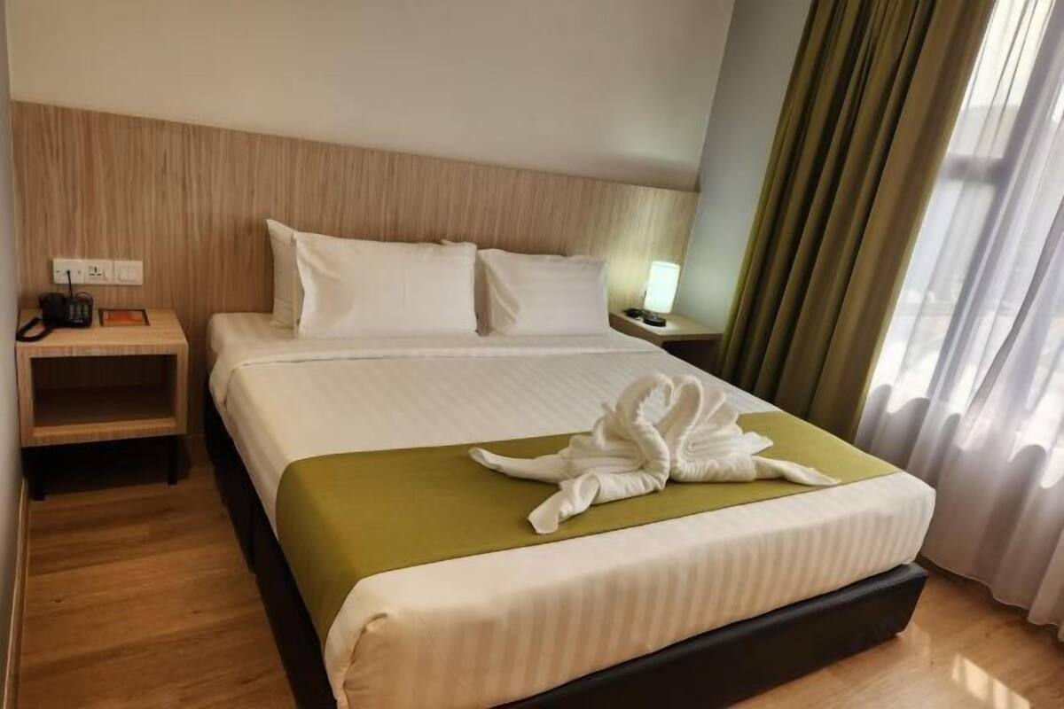 A hotel room with a bed, a bedside table, a lamp, and a window with curtains.