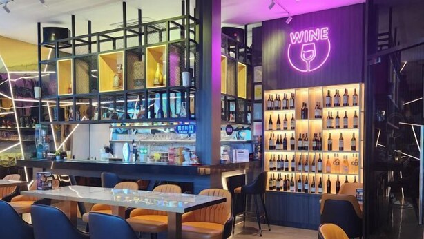 A modern bar area with a neon sign reading "WINE," shelves of wine bottles, and bar stools. - Hotel Marudu Inn (Kota Marudu)