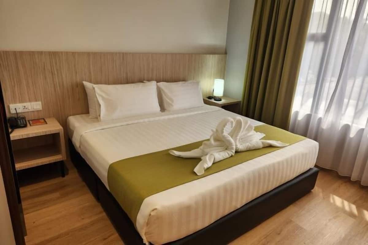 A hotel room with a bed, a nightstand, a lamp, and a window with curtains.