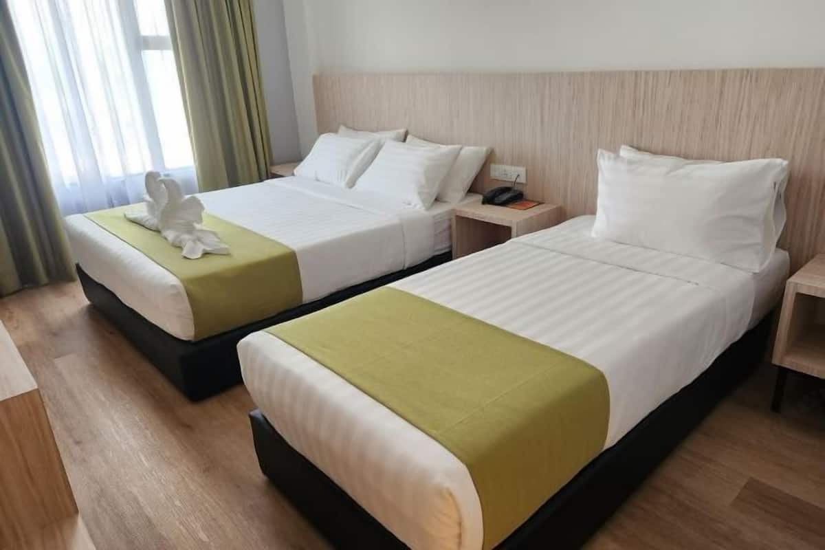 A hotel room with two beds, each with white linens and a green throw blanket.