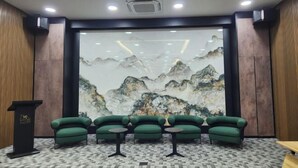 A conference room with a large mural of mountains, green upholstered chairs, and a podium. - Hotel Marudu Inn (Kota Marudu)