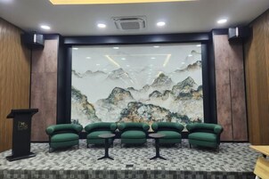 Un salón de conferencias con un gran mural de montañas, sillas tapizadas de verde y un atril.