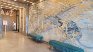 A lobby with marble walls, two teal benches, and a modern light fixture. - Hotel Marudu Inn (Kota Marudu)