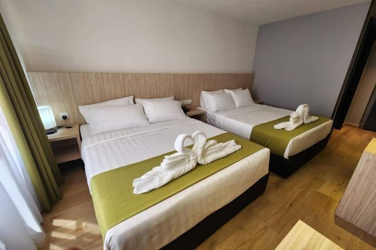 A hotel room with two beds, each with white linens and a green bedspread. There are towels arranged on the beds.