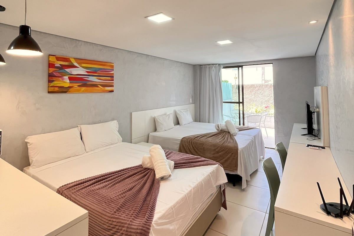 A modern hotel room with two beds, a desk, and a TV.