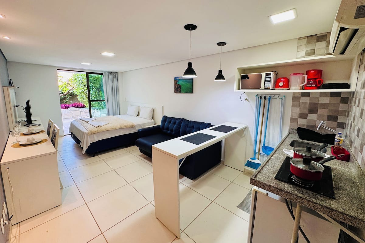 A compact hotel room with a bed, sofa, kitchenette, and a dining area.