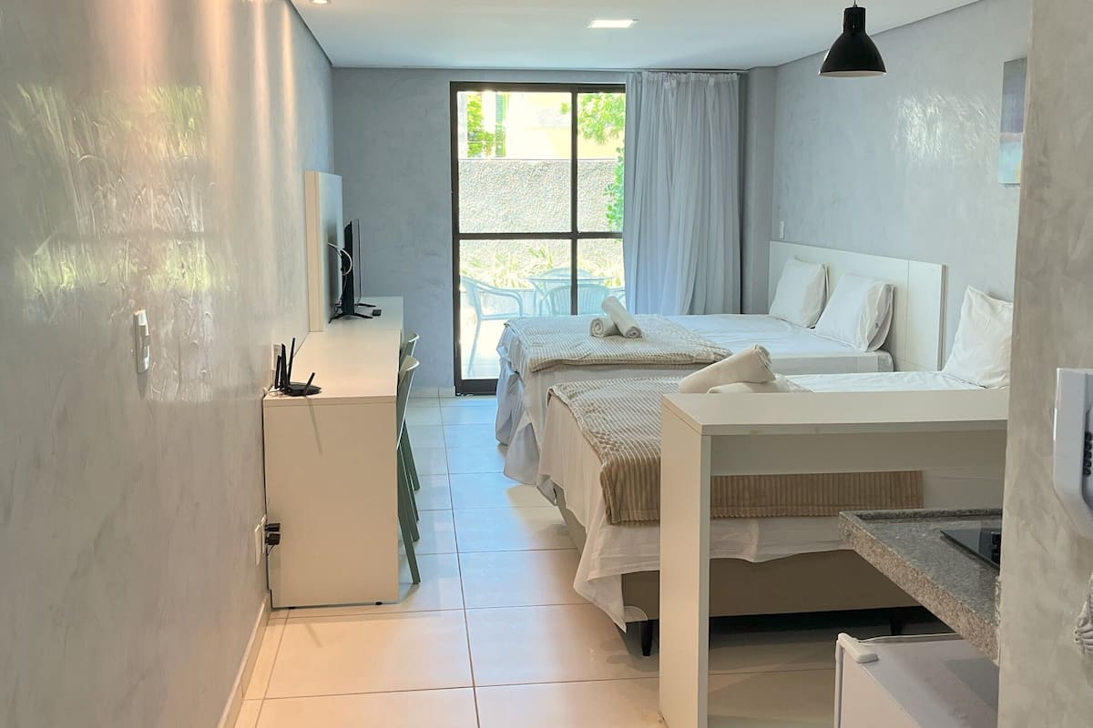A modern hotel room with a large bed, a desk, a chair, and a window with curtains.