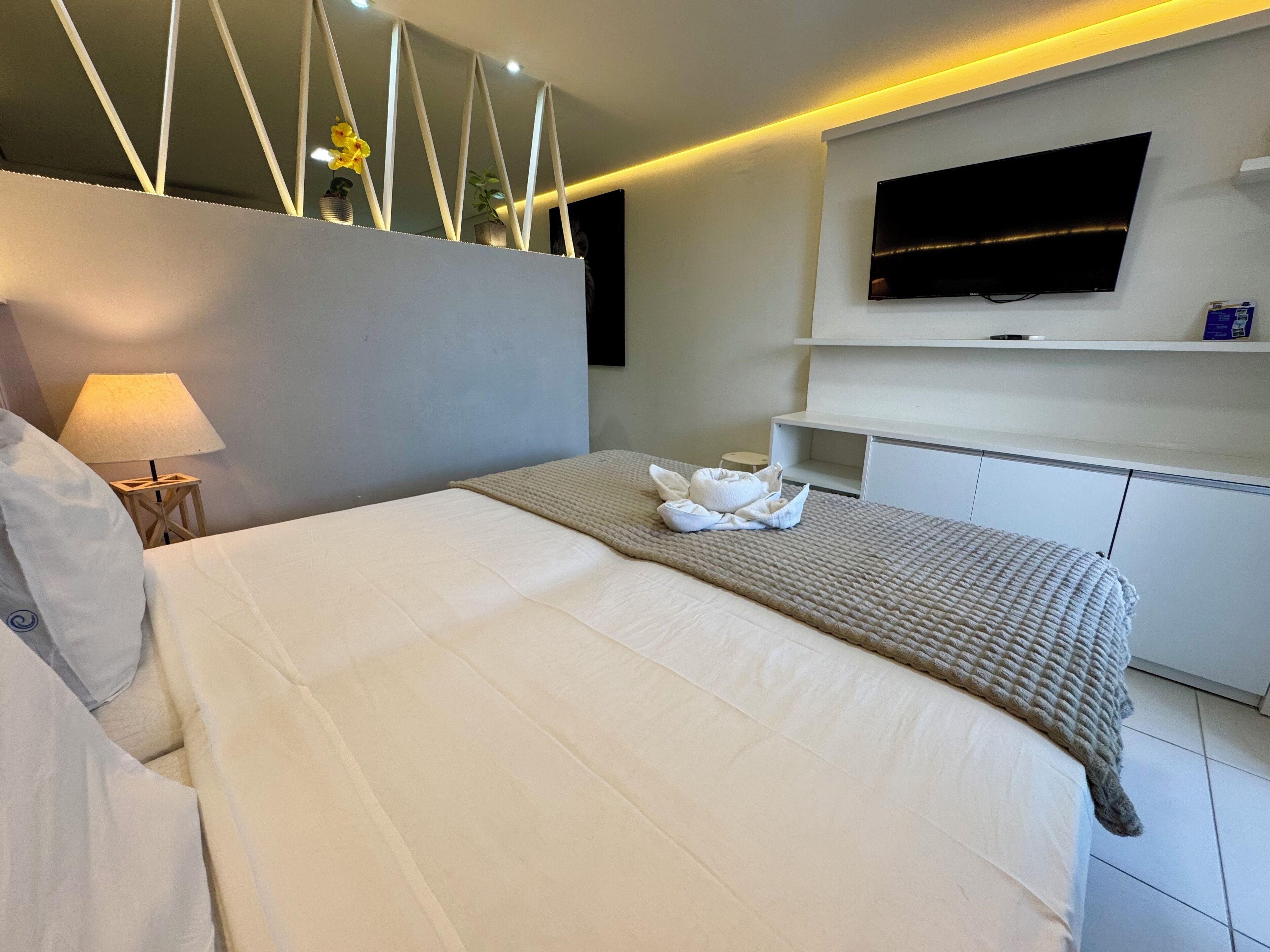 Una camera d'albergo moderna con un letto, una TV a parete, una lampada da comodino e un tavolino.