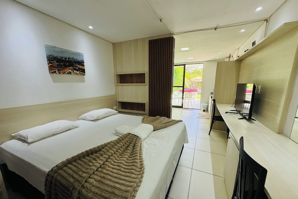 A hotel room with a bed, a desk, a television, and a view of the outdoors.