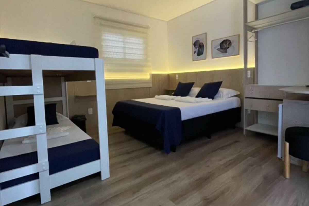 Une chambre d’hôtel de taille réduite, équipée de lits superposés, d’un lit simple, d’un bureau et d’une chaise.