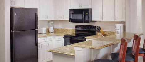 A kitchen with white cabinets, a black refrigerator, a microwave, a stove, and granite countertops.