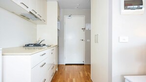 A narrow hallway with white cabinets and a wooden floor, leading to a closed door. - Skyline Studio Views on Spencer (Melbourne)