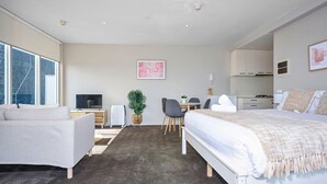 A modern hotel room with a large bed, a sofa, a desk, and a view of the city. - Skyline Studio Views on Spencer (Melbourne)
