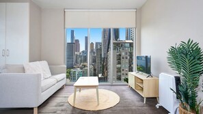 Een moderne woonkamer met uitzicht op de stad, een bank, een bijzettafeltje, een televisie en een radiator.