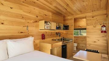 A wooden cabin interior with a bed, kitchenette, and a small bathroom.