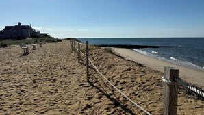 Una platja sorrenca amb una tanca de fusta i bancs, un edifici al fons i l'oceà.