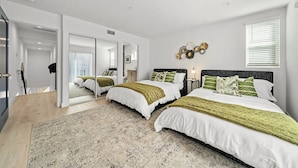 A modern bedroom with two beds, a large mirror, and a decorative wall piece. - Serene Escapes Hollywood  (Los Angeles)