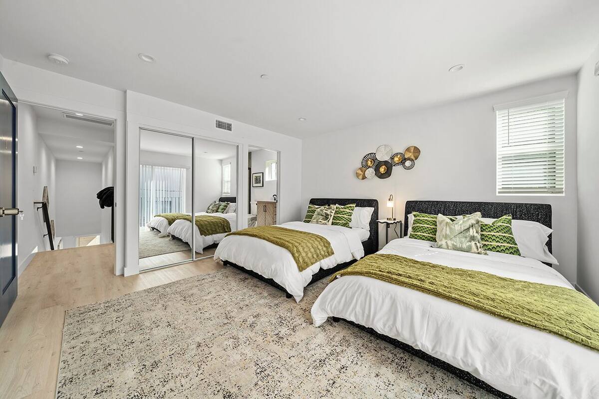 A modern bedroom with two beds, a large mirror, and a decorative wall piece.