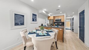 A modern kitchen with stainless steel appliances, a dining area with a round table and chairs, and a hallway leading to bedrooms. - Serene Escapes Hollywood  (Los Angeles)