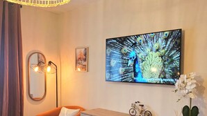 A bedroom with a bed, a wooden dresser, a chair, a mirror, a wall-mounted TV, and a hanging light fixture. - A change of scenery (Poitiers)
