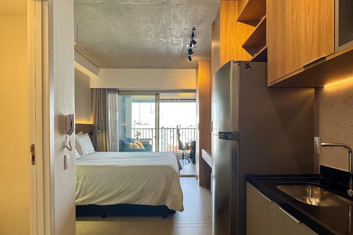 A hotel room with a bed, a kitchenette, and a view of the outside.