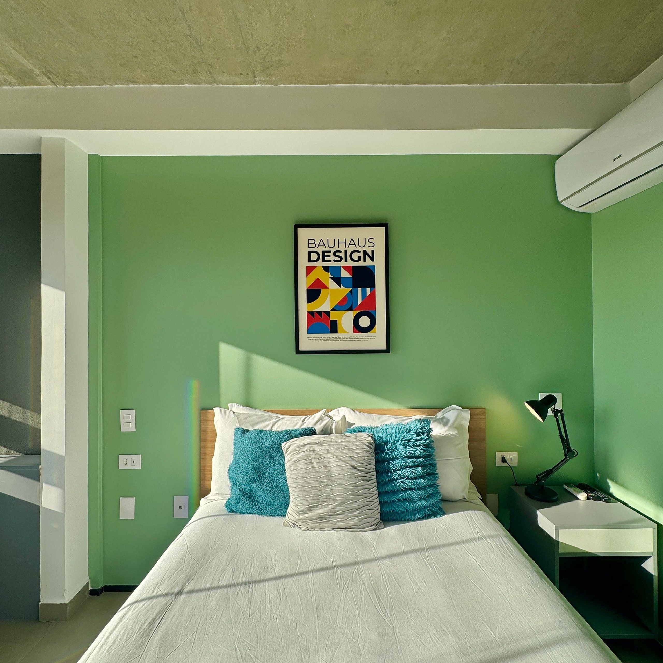Une chambre à coucher avec un lit, des oreillers, une table de chevet, une lampe et une affiche accrochée au mur.