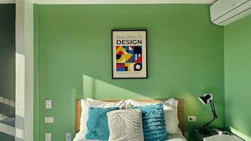 Une chambre à coucher avec un lit, des oreillers, une table de chevet, une lampe et une affiche accrochée au mur.