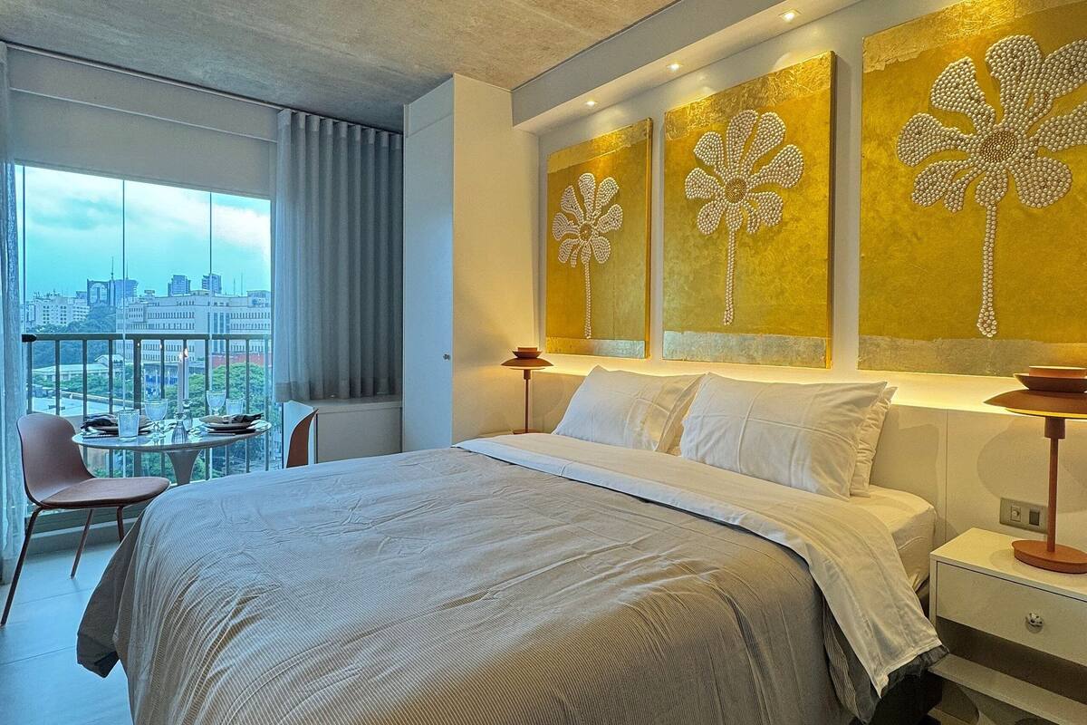 A modern hotel room with a large bed, a city view, and decorative wall art.