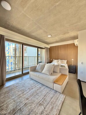 A modern hotel room with a large bed, a sofa, a small desk, and a view of a cityscape through large windows. - ON MELO ALVES (São Paulo)