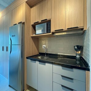 A modern kitchen with a stainless steel refrigerator, a microwave, and a black countertop. - ON MELO ALVES (São Paulo)