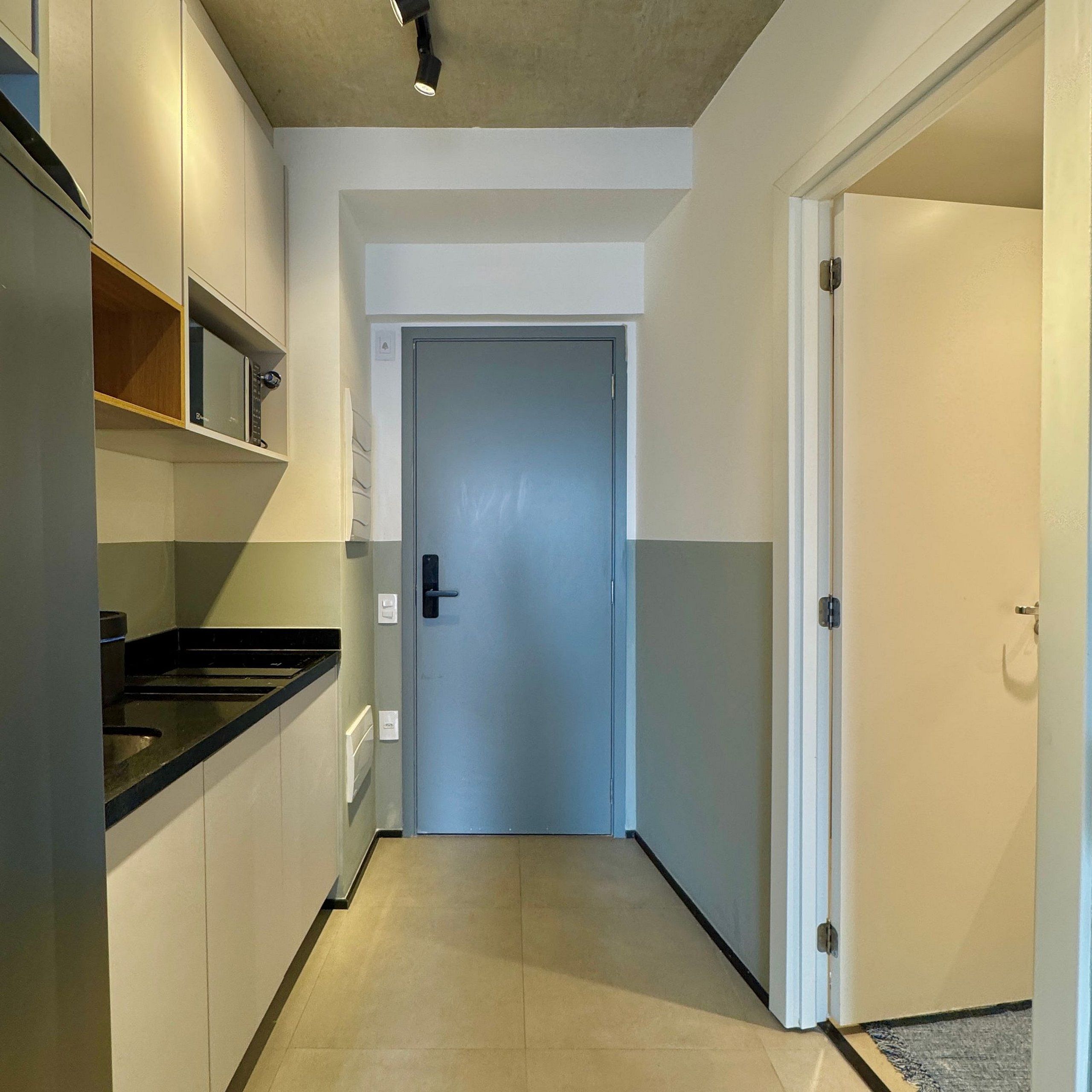 Un corridoio stretto con una porta in fondo, un forno a microonde a sinistra e un termostato al muro.