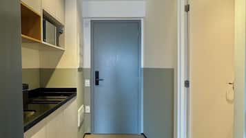 Un corridoio stretto con una porta in fondo, un forno a microonde a sinistra e un termostato al muro.