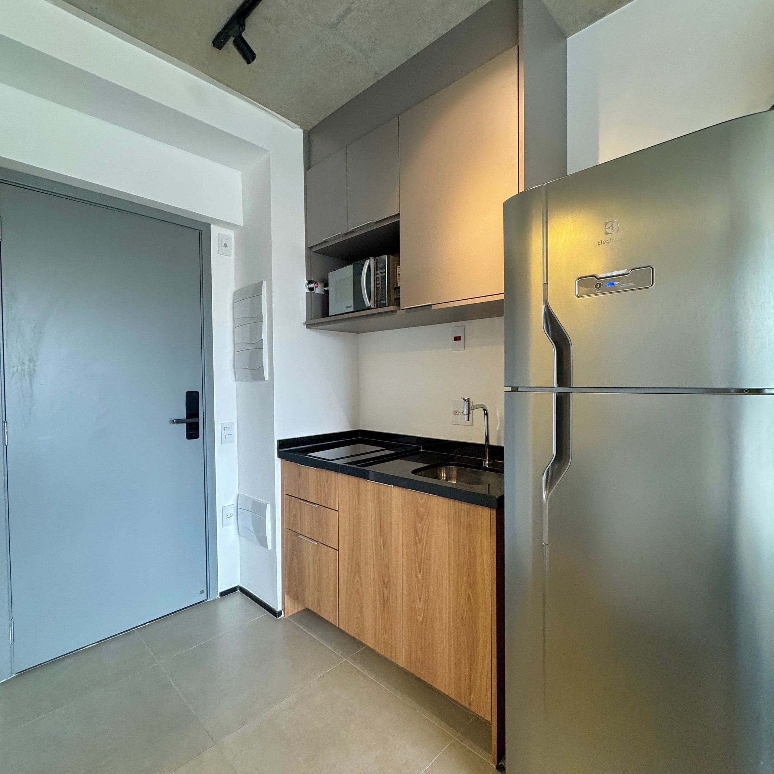 A modern kitchen with a stainless steel refrigerator, wooden cabinets, a black countertop, and a built-in microwave.