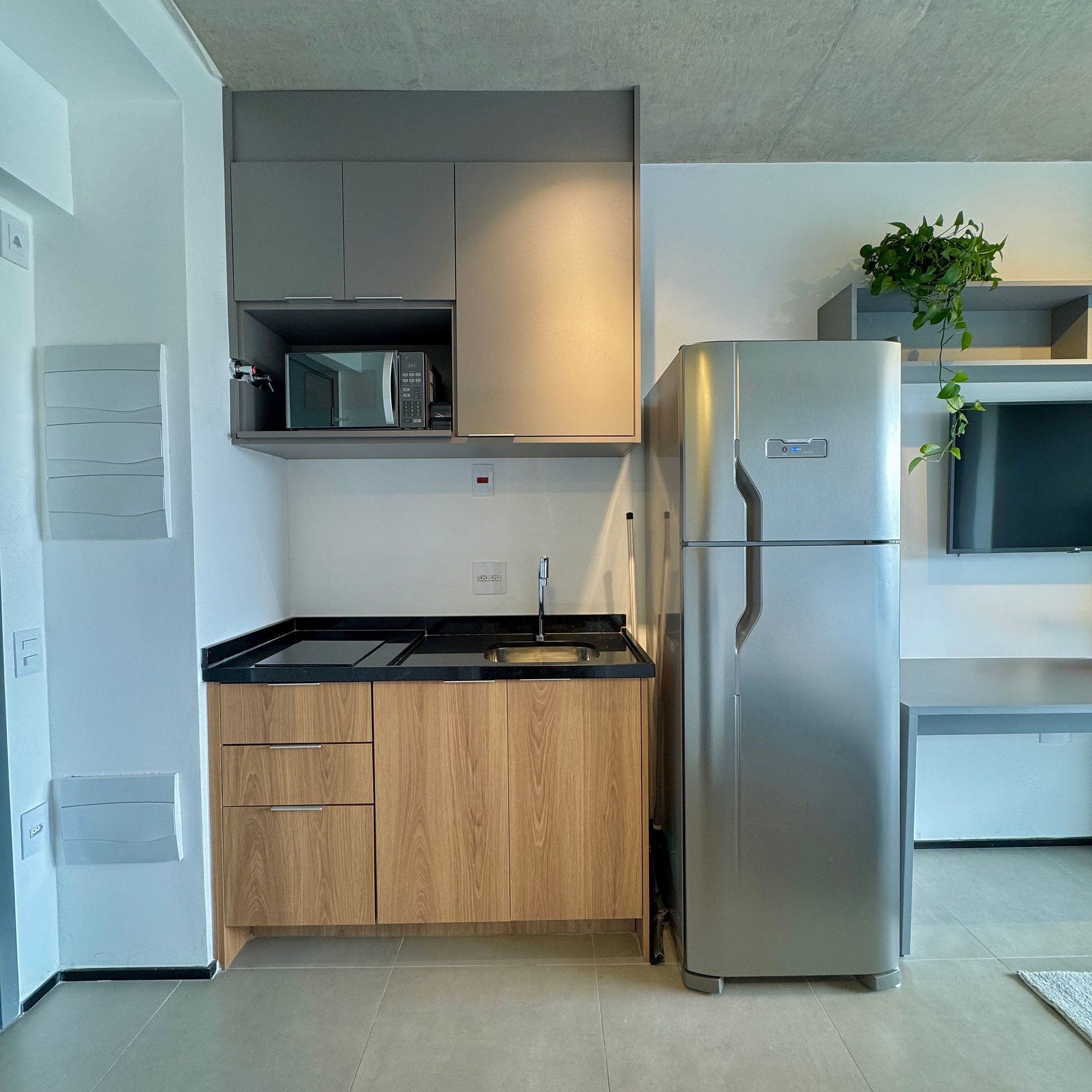 A modern kitchen with a stainless steel refrigerator, wooden cabinets, a microwave, and a sink.